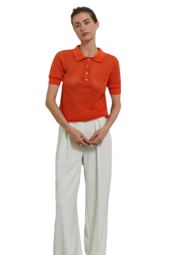 Polo en maille ajourée rouge orangé porté avec un pantalon large blanc