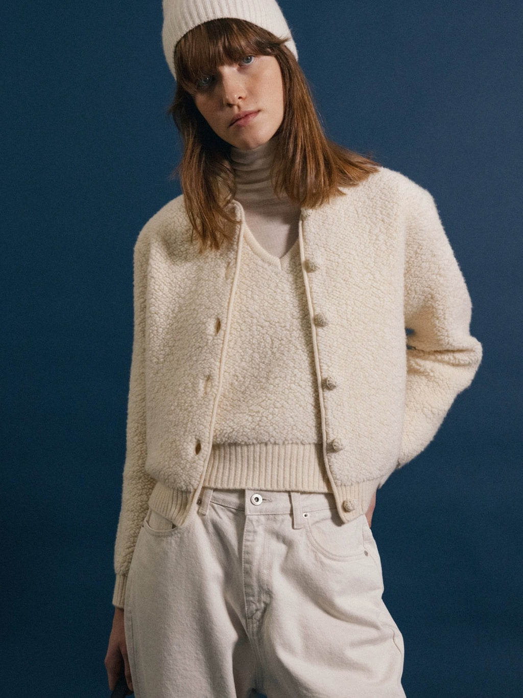 Veste courte en maille bouclette écru portée ouverte sur un col roulé et un pantalon large